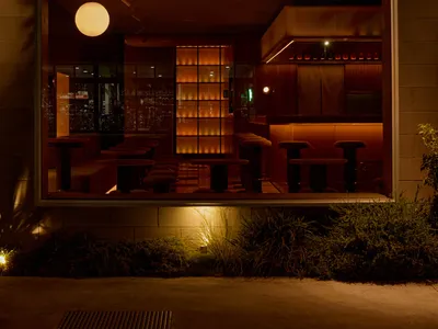 A modern restaurant bar with wooden interiors, glass walls, and metallic accents.