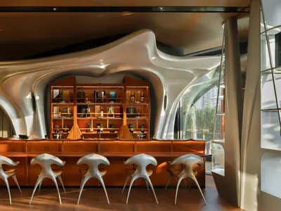 A modern bar with a futuristic, flowing counter and metallic stools.