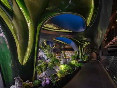 Modern restaurant interior with green metallic walls and illuminated plants.