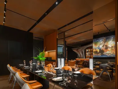 Modern, metallic-finished restaurant interior with black tables and orange chairs in a minimalist design.