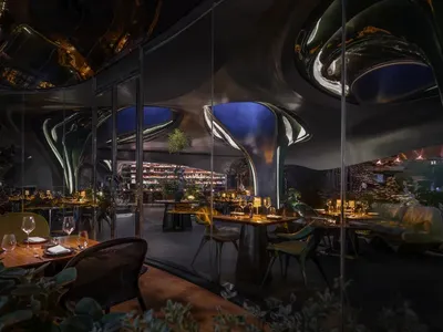 Modern restaurant interior featuring metallic structures, glass walls, and greenery