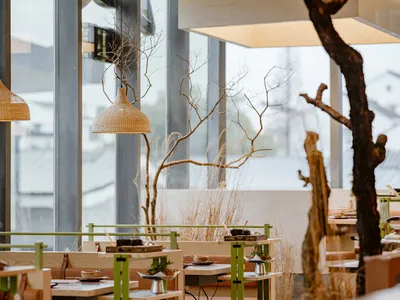 Modern restaurant interior with wooden tables, rattan light fixtures, and glass partitions.