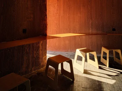 A cozy cafe interior featuring textured concrete walls and minimalist wooden stools.