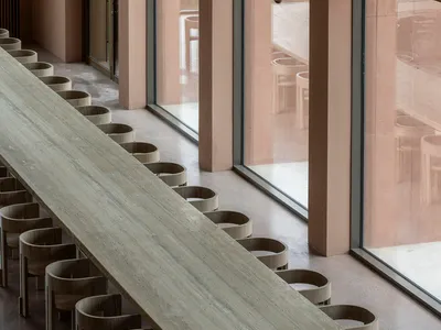 現代餐廳內，一排圓形木椅沿著長木桌排列。