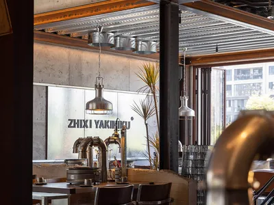 Industrial-style restaurant interior with exposed metal beams, concrete walls, and glass elements.
