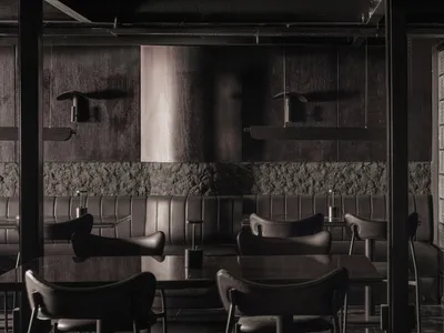 Modern restaurant interior with black leather dining chairs and concrete walls.