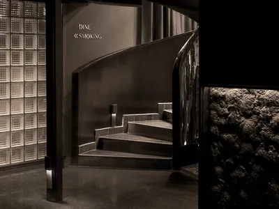 Interior design of a modern restaurant with black stairs and reflective metal wall.