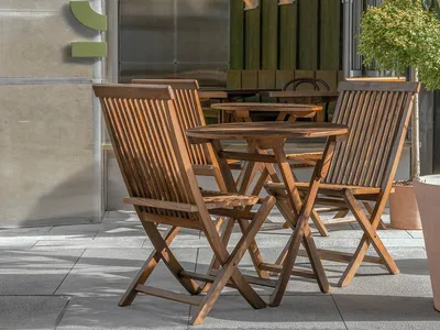 Outdoor seating area with wooden tables and chairs in front of a modern restaurant entrance.