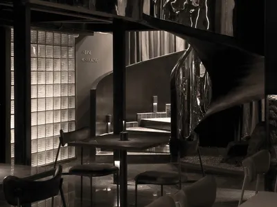 A modern restaurant interior with dark metallic elements and reflective surfaces, featuring tables, chairs, and a spiral stai