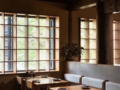 A modern restaurant interior with wooden tables, chairs, and a wooden floor.