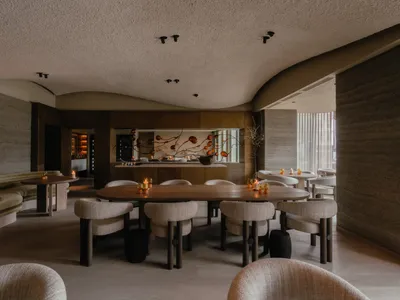 現代餐廳內部，配有木質餐桌、布面座椅，以及金屬吧檯的吧台區域。
