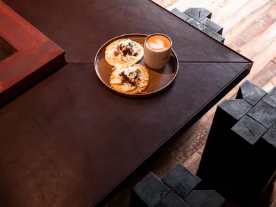 Plate of tacos and coffee cup on a wooden and leather table in a cafe setting.