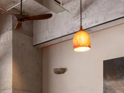 A modern, industrial-style restaurant with concrete and wooden elements, featuring a wooden ceiling fan and warm pendant ligh