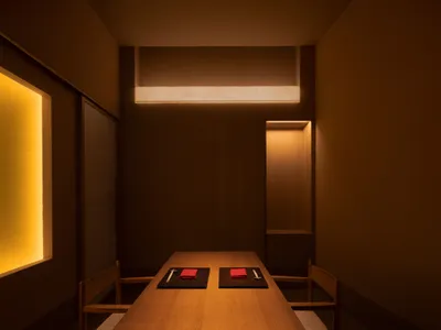 A modern restaurant dining room illuminated by warm, ambient lighting, featuring wooden furniture and minimalist decor.