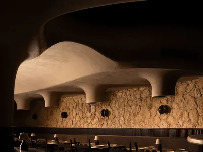 A modern restaurant interior with wooden tables, chairs, and stone walls.