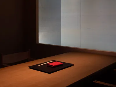 Minimalist dining room with wooden table and red napkin on a black placemat.