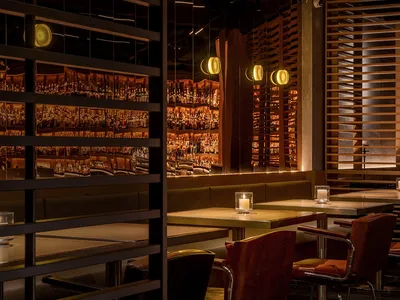 A modern restaurant bar with wooden tables, metal chairs, and a well-stocked back bar.
