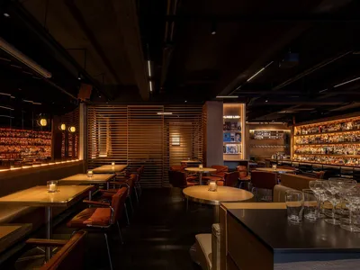 Modern restaurant bar with wooden accents, glass shelves, and stainless-steel countertops.