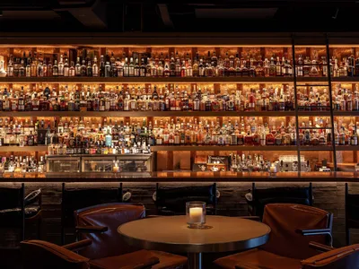 Industrial-style restaurant bar with wooden seating, metal tables, and glass bottles in the background.
