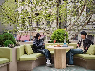 Two individuals sitting at a round table in a modern restaurant with concrete furnishings and greenery.