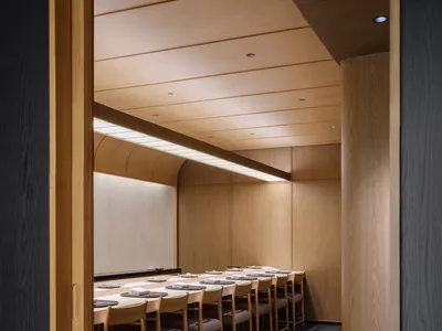 A minimalist restaurant interior featuring wooden tables and chairs with white tablecloths and plates.