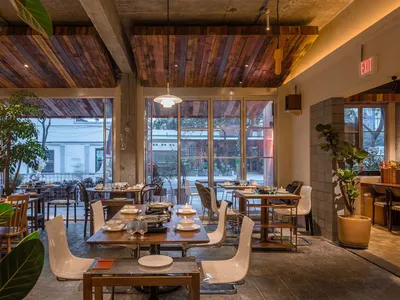 Interior view of a cafe with wooden tables, concrete walls, and indoor plants.