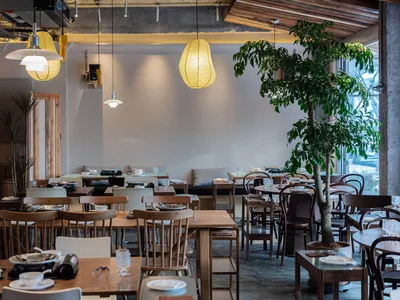 Industrial restaurant interior with wooden tables, concrete walls, glass windows, and hanging paper lanterns.