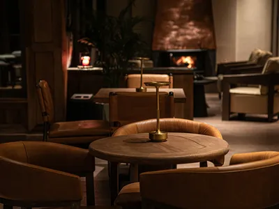 A cozy restaurant interior with leather chairs, walnut tables, and a warm copper fireplace.