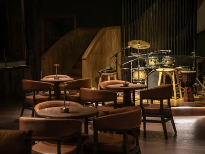 A modern restaurant interior featuring wooden tables, leather chairs, and metal drum set.