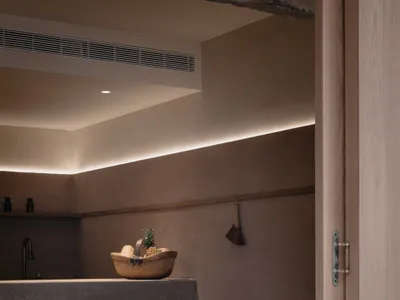 A minimalist residential kitchen with wood and concrete materials, featuring a basket of fruits and a vintage table and chair