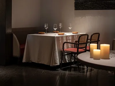 A minimalist restaurant interior featuring wooden tables, leather chairs, and a stone floor.