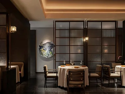 A modern restaurant interior with a table setting featuring wine glasses, plates, and bowls on a round table covered in a whi