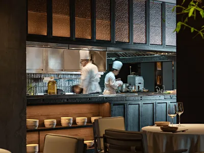 A modern restaurant kitchen with open concept design, featuring wooden materials and chefs preparing food.