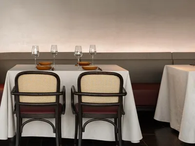 A modern restaurant dining room with white tablecloths, wooden chairs, and minimalist decor.