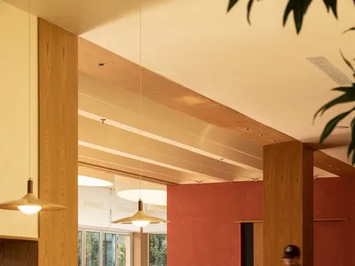 A modern cafe interior with wooden tables and chairs, red walls, and a counter area.