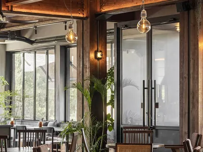 Restaurant interior with wooden tables and chairs, industrial lighting, and greenery.