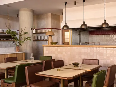 A modern restaurant interior featuring tables and chairs with wooden frames and green leather seats, set against a backdrop o