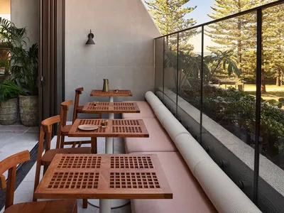 A modern restaurant balcony featuring wood furniture, concrete walls, and glass railings overlooking greenery.