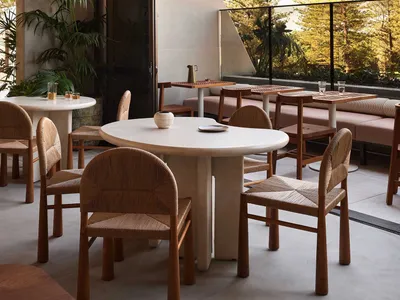 Circular dining tables with woven chairs on a patio made of concrete, surrounded by lush greenery and trees.