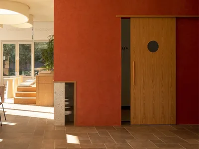 An interior space featuring modern decor, including a red wall, wooden elements, and a corridor leading to a bathroom.