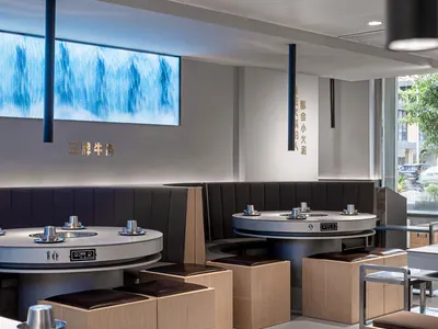 A modern restaurant interior with wooden tables, metal booths, and fabric seating.
