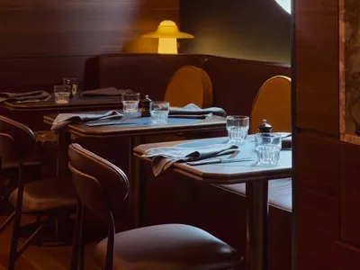 Modern restaurant interior featuring wooden tables and chairs, with a warm yellow light source and a contemporary design aest