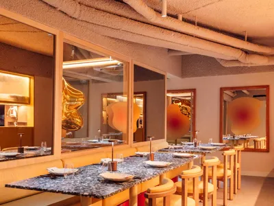 A modern restaurant interior with marble tables, wooden chairs, and glass windows.