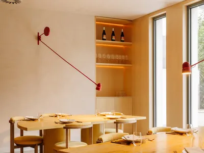 Modern restaurant interior featuring wooden tables and chairs with concrete flooring and walls.