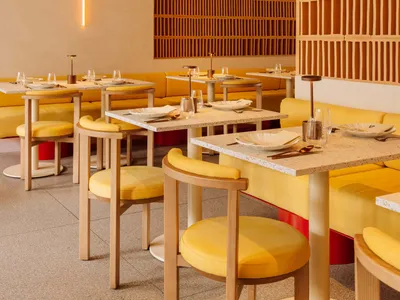 Modern restaurant interior with yellow seating, concrete walls, and wooden accents