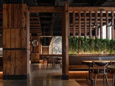 Industrial-themed restaurant interior with wooden elements and hanging green plants.