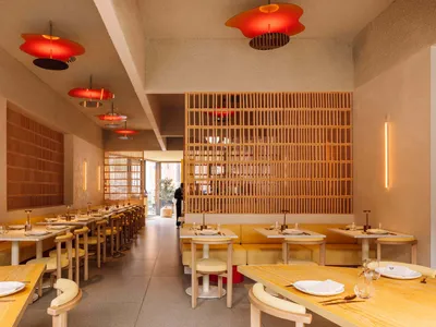 A modern restaurant interior with wooden tables, chairs, and booths. The space features contemporary design elements and an i