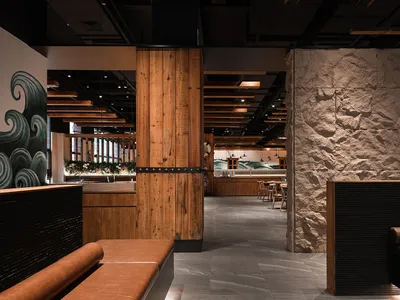 A stylish modern restaurant interior featuring wooden furniture, stone walls, and leather seating.
