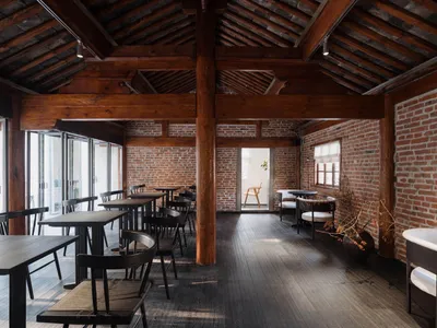 Industrial-style restaurant interior with wooden tables, brick walls, and exposed wooden beams on the ceiling.