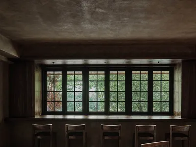 An industrial-themed restaurant bar with rustic wood tables and chairs, metallic accents, and a large window overlooking tree